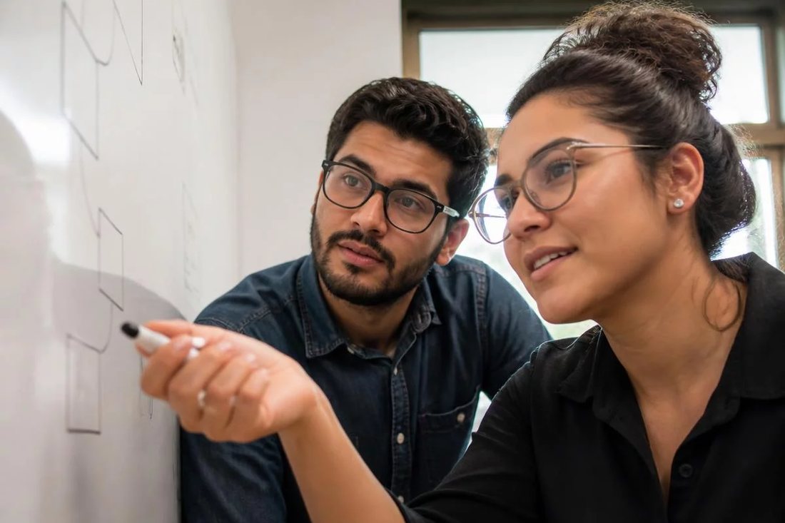 Facilitadora aponta para um mapa de argumento desenhado no quadro branco enquanto um participante acompanha